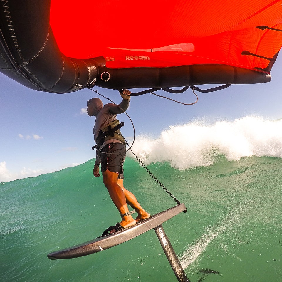 A Wing Foiler dropping into a wave, effortlessly draws out a bottom turn, supported by the robust Cedrus Evolution Wind mast, designed to endure the extreme forces of wind and water. The mast demonstrates its superior strength and resilience, essential for withstanding the dynamic pressures of high-speed wind-foiling.