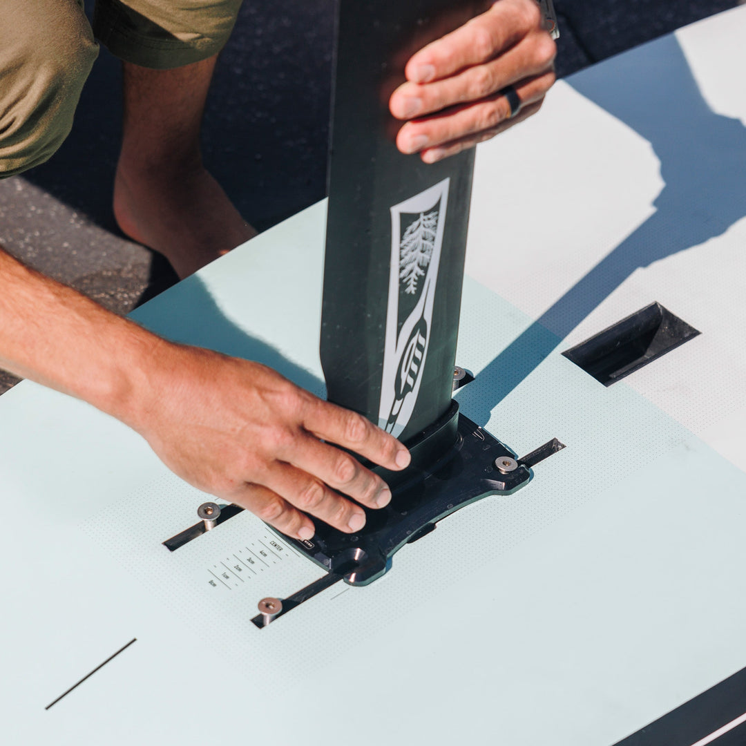Hands secure a Cedrus Evolution Wind mast to a board, showcasing the mast’s robust engineering designed to withstand the rigorous demands of wind-foiling. The key attributes include superior torsional stiffness for optimal control, a patented ventilation-resistant design for enhanced stability, and compatibility with various foil systems thanks to its precision machined adapters. This process highlights the user-friendly installation that complements the mast's advanced technical specifications.
