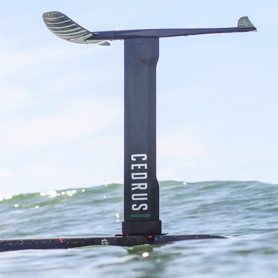 A surfboard floating upside down on the ocean with the foil out of the water. Demonstrates different hydrofoils working with the same Cedrus mast to show compatibility of the Cedrus mast across all major foil brands.