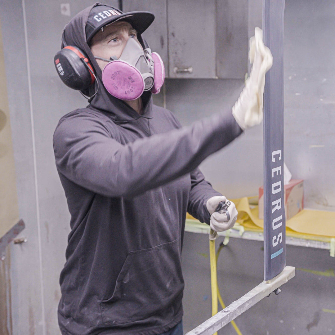 Person in a spray booth with protective gear, holding a spray gun with 'CEDRUS' branding.