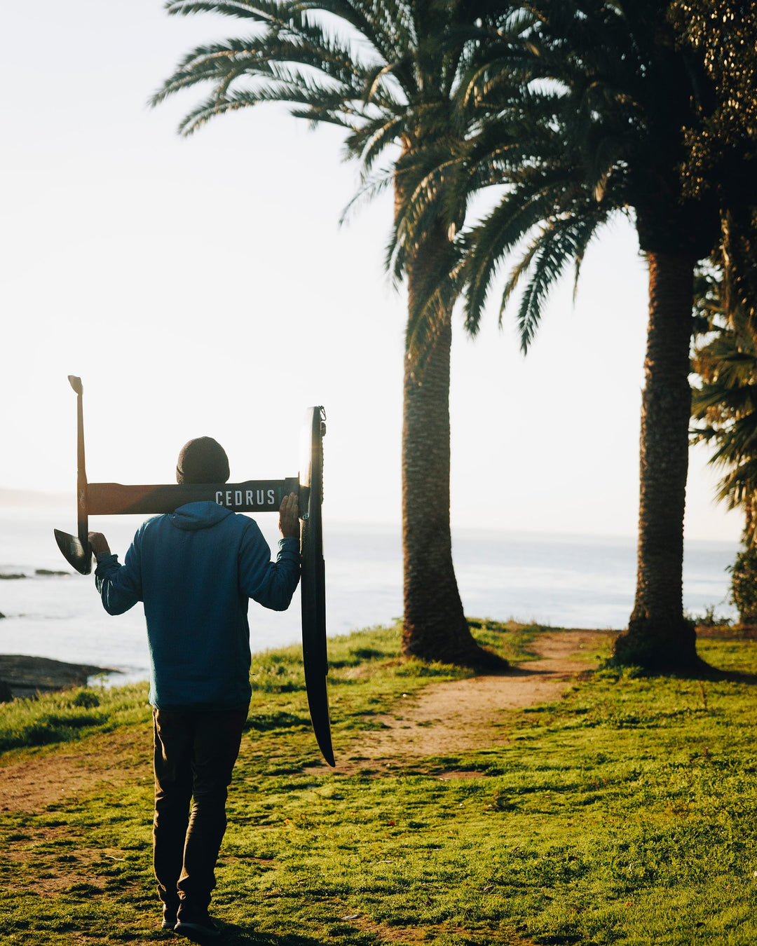 Person looking out over a cliff holding a foil board with a Cedrus mast. Cedrus hydrofoil's hollow architecture, showcasing lightweight design without compromising on strength, tailored for passionate foilers and beginners alike.