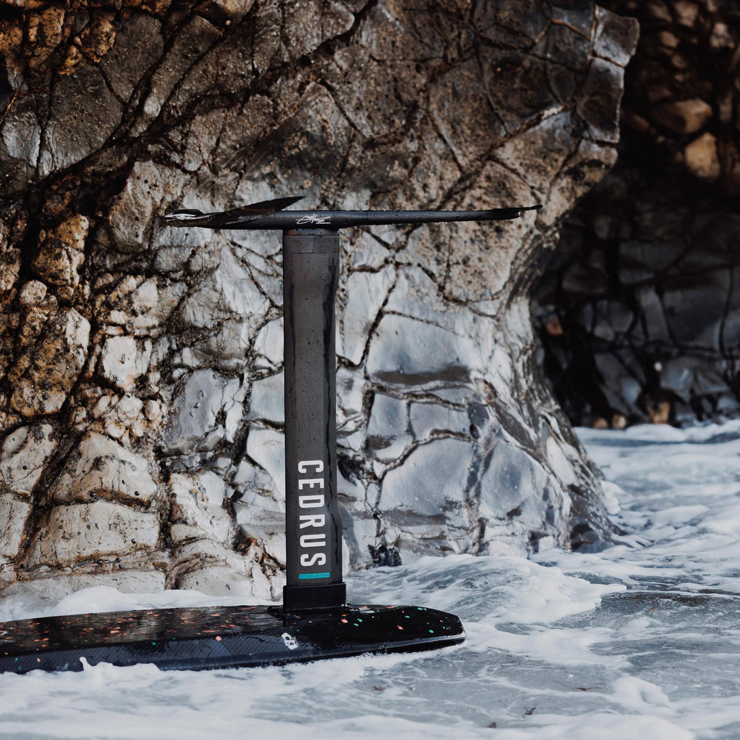  Positioned upright against a rock-strewn cliff, the Cedrus Evolution Surf Mast stands as a testament to the precision engineering that offers riders less drag and more dynamic turns in surf foiling.