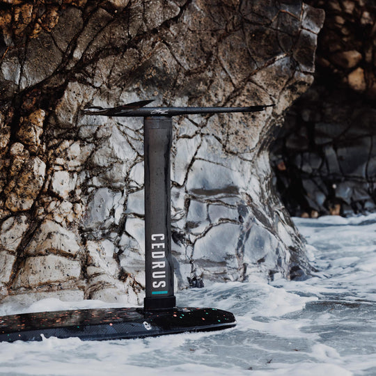  Positioned upright against a rock-strewn cliff, the Cedrus Evolution Surf Mast stands as a testament to the precision engineering that offers riders less drag and more dynamic turns in surf foiling.