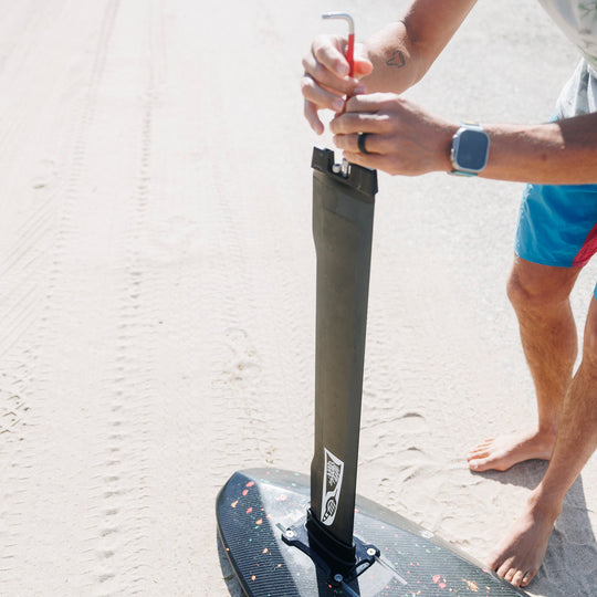 A person assembling an Armstrong foil on a Cedrus Evolution Surf mast using a Cedrus Foil Adapter for the brand of Armstrong foils, highlighting its sleek black design and robust construction with dual stainless steel posts for secure mounting. It exemplifies Cedrus' commitment to versatile, universal and seamless foil compatibility and advanced engineering