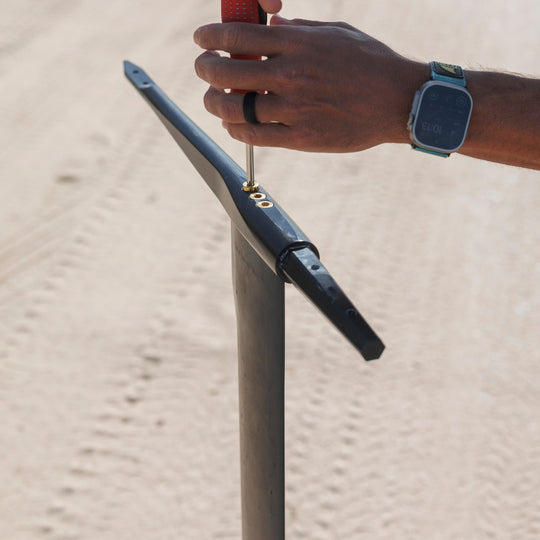 A person assembling an Armstrong foil on a Cedrus Evolution Surf mast using a Cedrus Foil Adapter for the brand of Armstrong foils, highlighting its sleek black design and robust construction with dual stainless steel posts for secure mounting. It exemplifies Cedrus' commitment to versatile, universal and seamless foil compatibility and advanced engineering