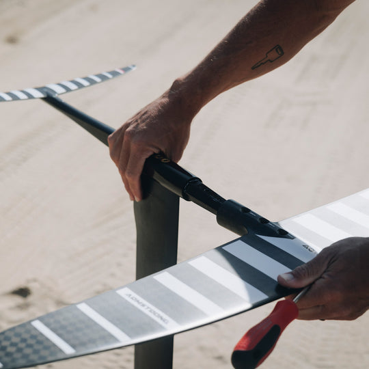 A person assembling an Armstrong foil on a Cedrus Evolution Surf mast using a Cedrus Foil Adapter for the brand of Armstrong foils, highlighting its sleek black design and robust construction with dual stainless steel posts for secure mounting. It exemplifies Cedrus' commitment to versatile, universal and seamless foil compatibility and advanced engineering