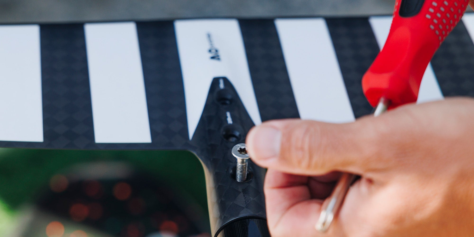 Hand meticulously fastening a screw on a hydrofoil, showcasing the precision and quality of Cedrus accessories, including shims, durable hardware, and specialized foil tools for optimal performance and maintenance.