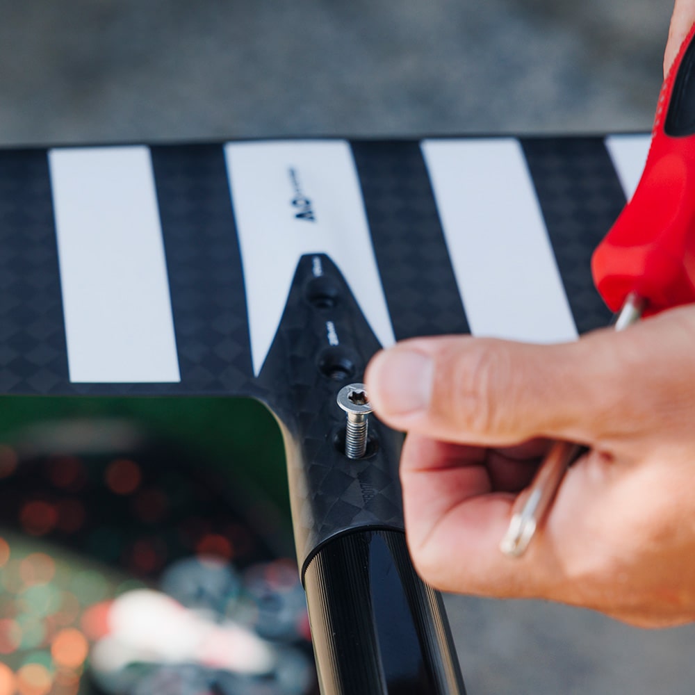 Hand meticulously fastening a screw on a hydrofoil, showcasing the precision and quality of Cedrus accessories, including shims, durable hardware, and specialized foil tools for optimal performance and maintenance.