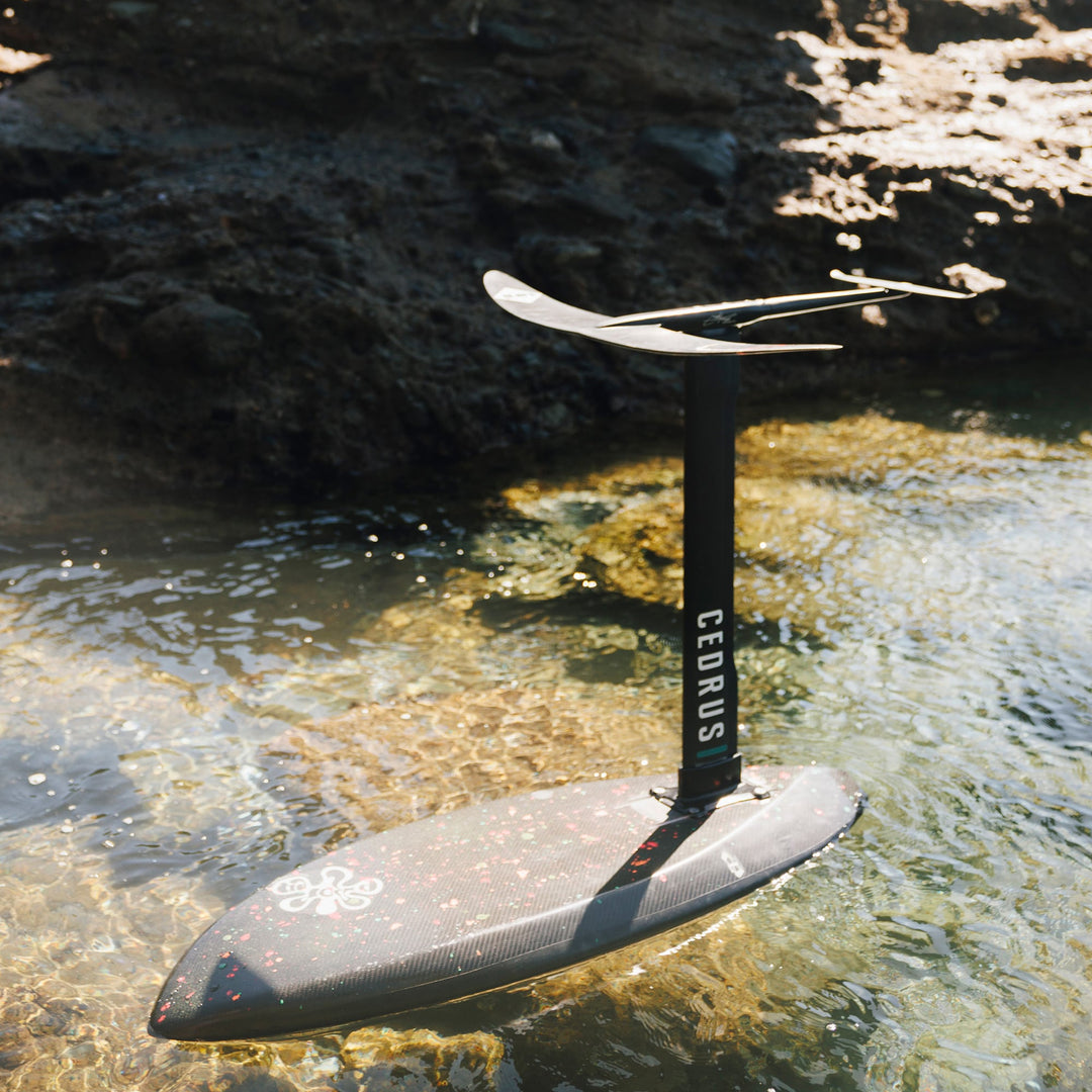 Partially submerged in clear waters, the Cedrus Evolution Surf Mast attached to a board demonstrates its readiness for action and the fluidity it brings to the surfing experience.