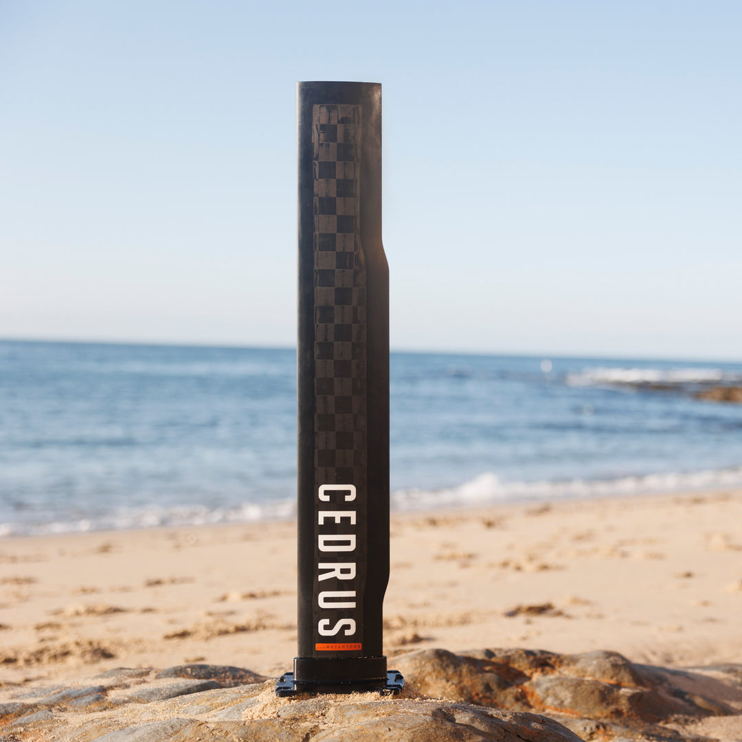 The Cedrus Evolution Wind mast is perfectly poised on sandy shores, with its distinctive checkered carbon fiber showing the meticulous engineering behind this icon of wind-foiling stability