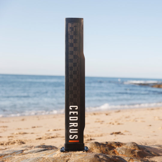 The Cedrus Evolution Wind mast is perfectly poised on sandy shores, with its distinctive checkered carbon fiber showing the meticulous engineering behind this icon of wind-foiling stability